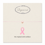 A pink wish necklace with a single pearl bead on a thin pink string, displayed on a cream-colored textured card. The card features the 'Dogeared' brand logo at the top and a pink ribbon graphic with the text 'the original wish necklace' at the bottom.