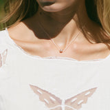 A close-up lifestyle shot of a model wearing a delicate silver chain necklace with a small, round rose gold bead pendant. The model is wearing a white top with a butterfly design on the front, set against a softly blurred green background.